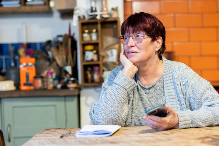 Older women in home kitchen holding phone